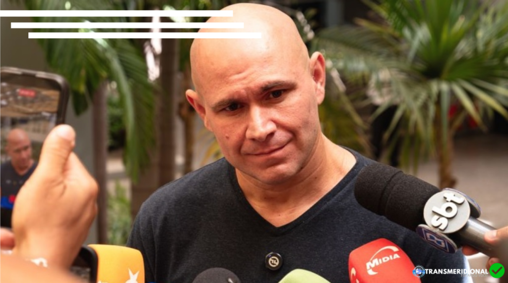 Foto em close do prefeito de Cuiabá, Abílio Brunini, em entrevista a inúmeros órgãos de imprensa. Ao fundo folhagens de palmeira anã, verdes.
