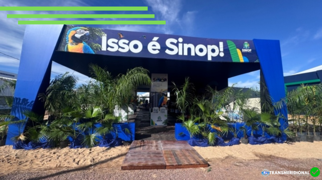 Estande azul, escrita "isso é Sinop". Plantas e estrados de madeira, céu azul.
